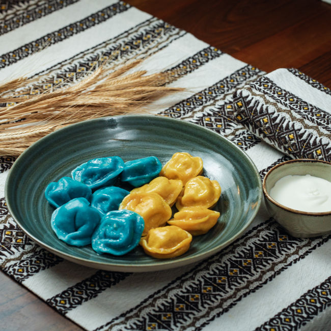 Teigtaschen in Farbe Blau Gelb auf dem Teller und daneben Teller mit Sahne